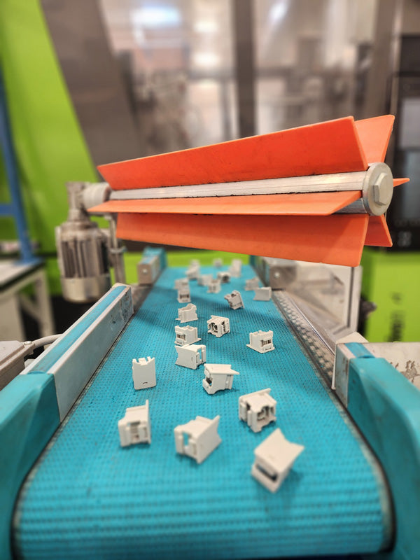 Small plastic parts on a conveyor belt under an orange divider in an injection molding facility.